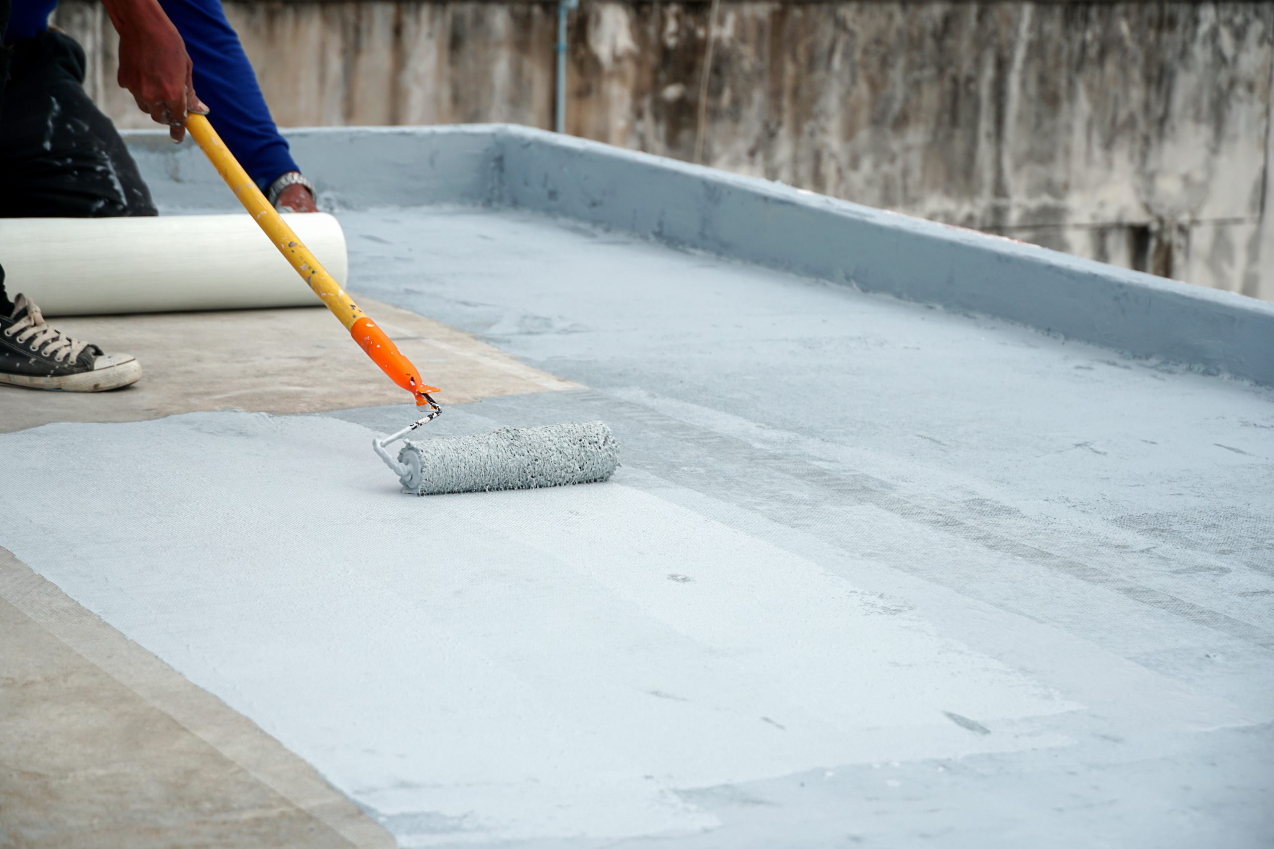 Waterproofing coating being rolled onto a terrace slab over fibre mesh